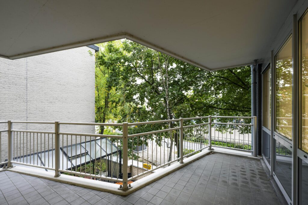 Overdekt balkon met metalen balustrade en uitzicht op bomen aan de Prins Hendrikkade.